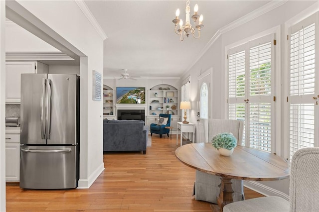 dining space featuring crown molding, a glass covered fireplace, ceiling fan with notable chandelier, and light wood-style flooring