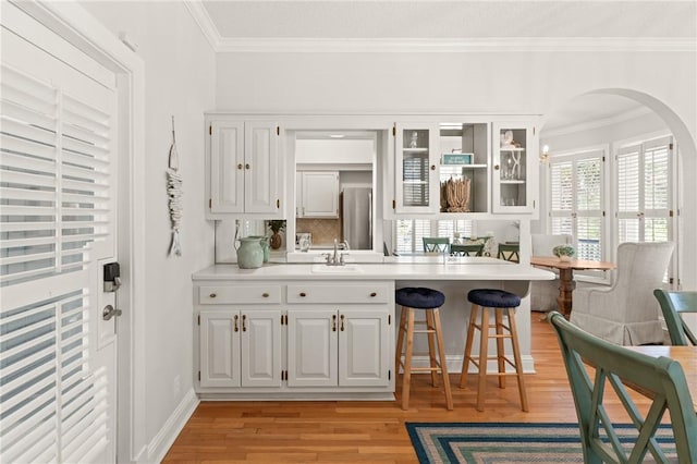 bar featuring decorative backsplash, ornamental molding, arched walkways, a sink, and light wood finished floors