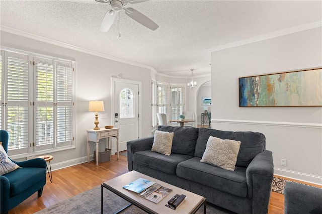 living area with light wood-type flooring, ornamental molding, baseboards, and ceiling fan with notable chandelier