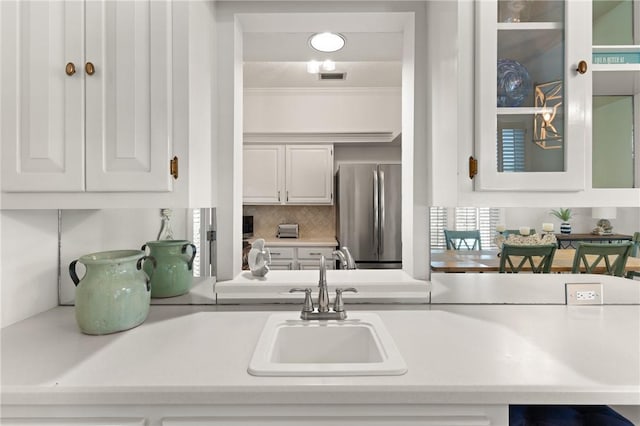 kitchen with visible vents, a sink, light countertops, freestanding refrigerator, and white cabinetry