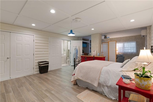 bedroom with a ceiling fan, a wall mounted AC, connected bathroom, light wood-style floors, and recessed lighting