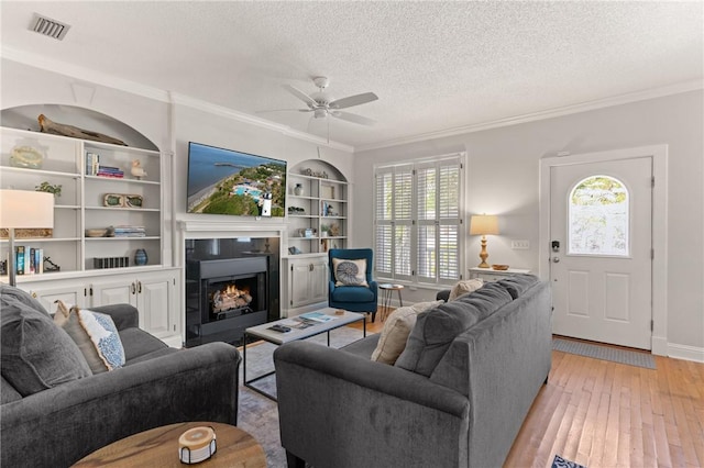 living room with a ceiling fan, a textured ceiling, visible vents, light wood finished floors, and ornamental molding