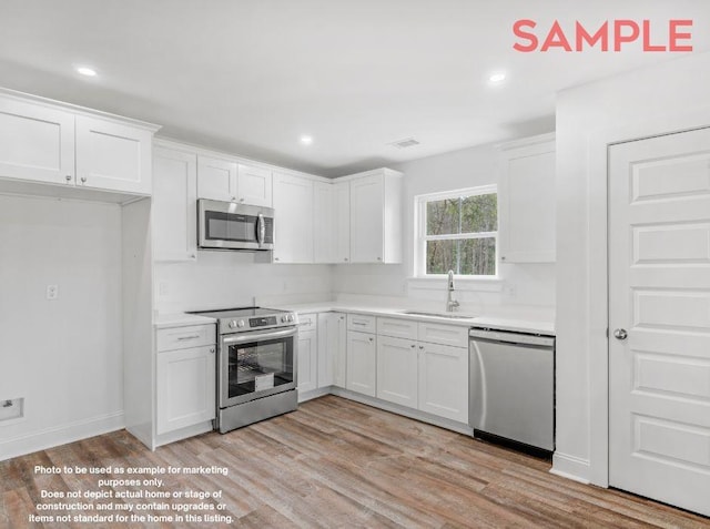 kitchen featuring appliances with stainless steel finishes, light wood-type flooring, white cabinetry, and sink