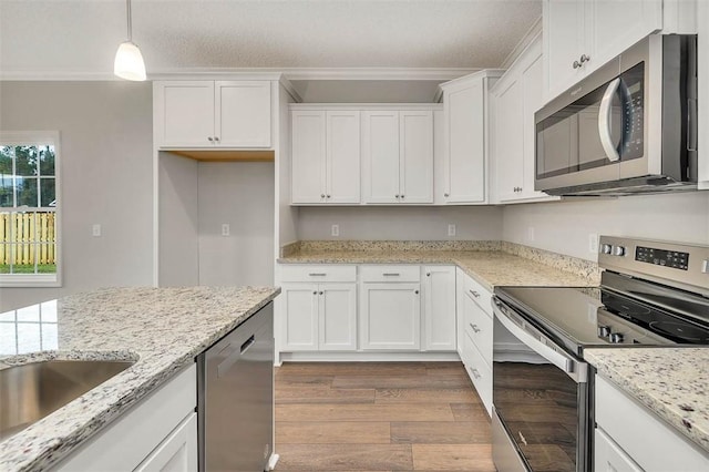 kitchen featuring stainless steel appliances, white cabinetry, hanging light fixtures, and ornamental molding