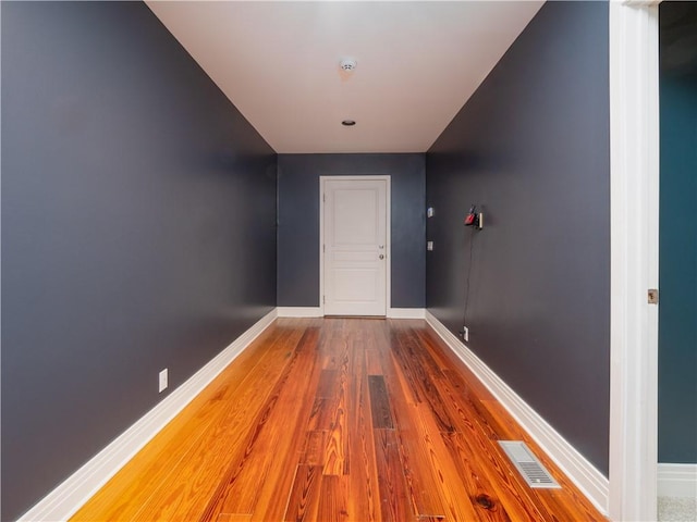 hall featuring baseboards, visible vents, and wood finished floors