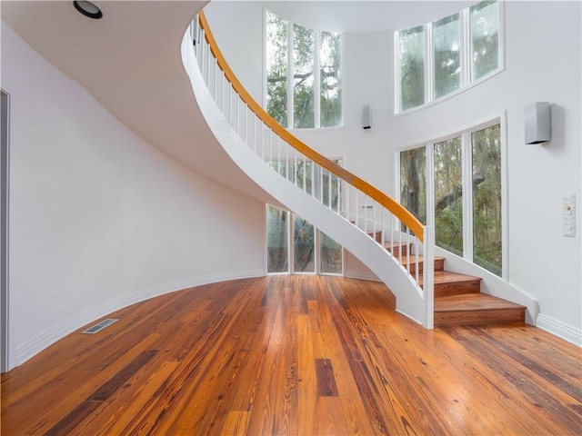staircase featuring a high ceiling, baseboards, visible vents, and wood-type flooring