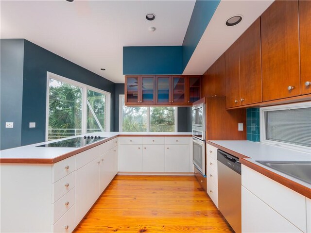 kitchen featuring light countertops, a peninsula, glass insert cabinets, stainless steel appliances, and light wood-style floors