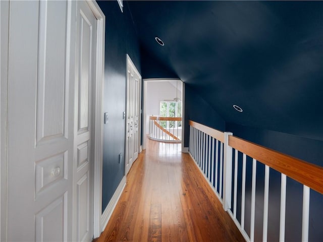 corridor with hardwood / wood-style flooring, lofted ceiling, and baseboards
