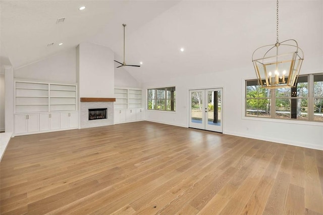 unfurnished living room featuring built in features, high vaulted ceiling, light hardwood / wood-style floors, ceiling fan with notable chandelier, and french doors