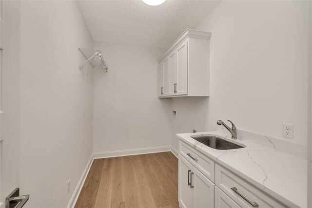 laundry area with sink, cabinets, a textured ceiling, light wood-type flooring, and hookup for a washing machine