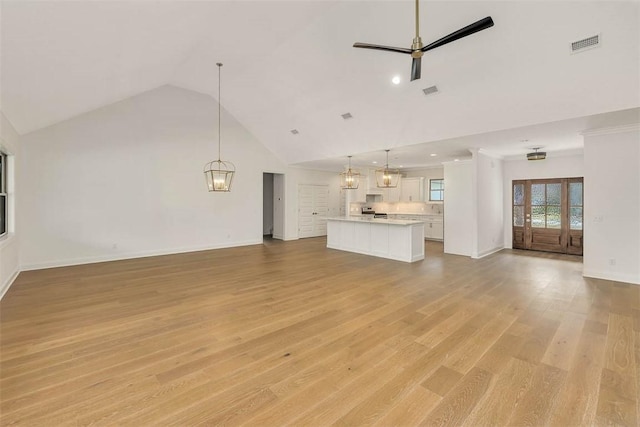 unfurnished living room with high vaulted ceiling, light hardwood / wood-style floors, and ceiling fan with notable chandelier