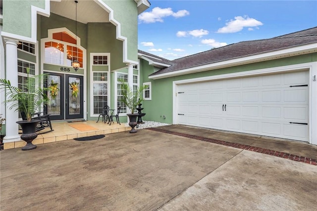 property entrance with stucco siding, french doors, driveway, and roof with shingles