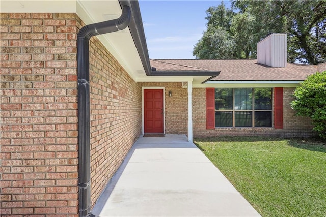 300 Bushoan Rd, Brunswick, GA 31525 - view of exterior entry featuring brick siding, roof with shingles, a yard, and a chimney