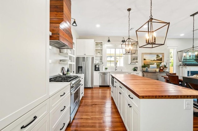 kitchen with dark wood-type flooring, butcher block countertops, custom range hood, stainless steel appliances, and a sink