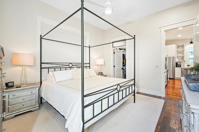 bedroom featuring stainless steel refrigerator, a closet, wood-type flooring, baseboards, and a spacious closet