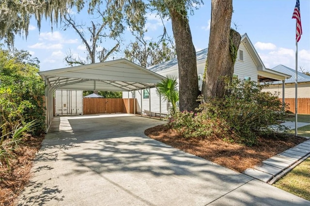 view of side of home featuring a detached carport, concrete driveway, and fence