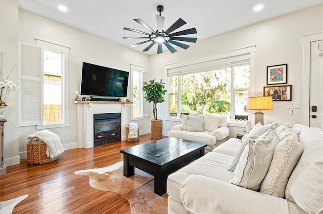 living area with a glass covered fireplace, recessed lighting, baseboards, and wood finished floors