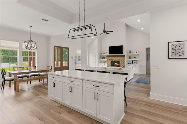 kitchen featuring a fireplace, ceiling fan, a center island, white cabinets, and crown molding