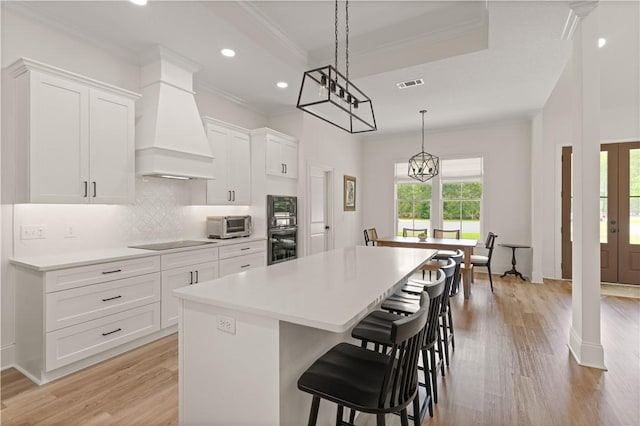 kitchen featuring crown molding, a kitchen island, custom exhaust hood, black electric stovetop, and light wood finished floors