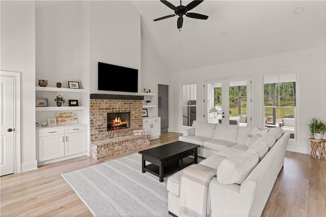 living room featuring high vaulted ceiling, ceiling fan, light wood-style floors, a fireplace, and french doors