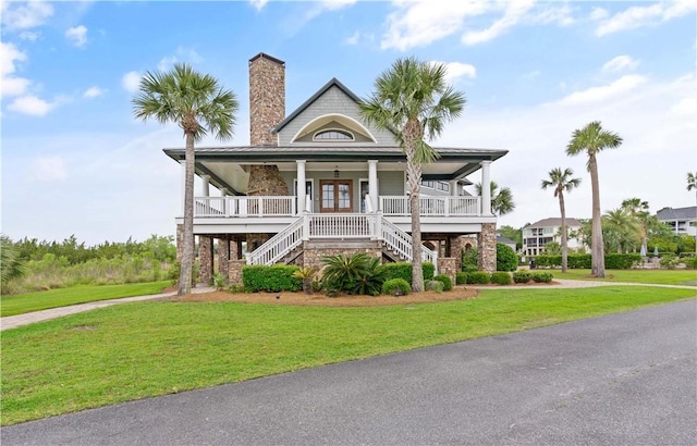 beach home with stairs, covered porch, french doors, a front yard, and a chimney