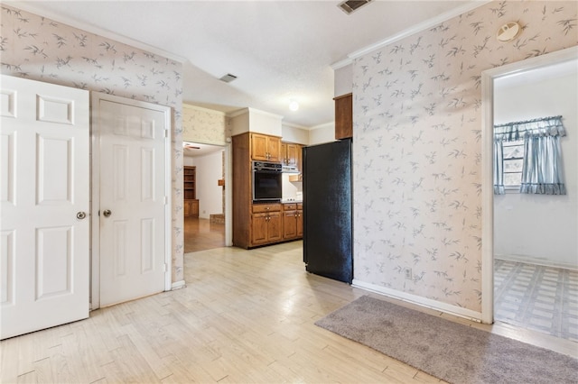 kitchen featuring brown cabinets, crown molding, light wood-type flooring, black appliances, and wallpapered walls