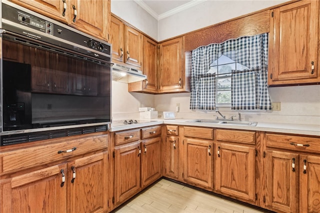 kitchen with oven, under cabinet range hood, a sink, ornamental molding, and brown cabinets