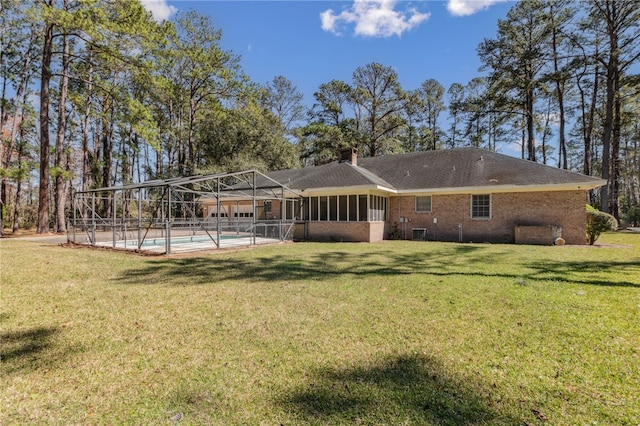 rear view of property with an outdoor pool, a chimney, a lanai, a yard, and brick siding