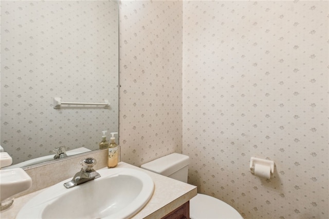 half bathroom featuring vanity, toilet, and wallpapered walls