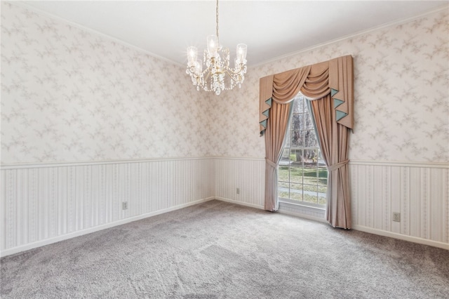 carpeted empty room featuring wallpapered walls, ornamental molding, a notable chandelier, and wainscoting