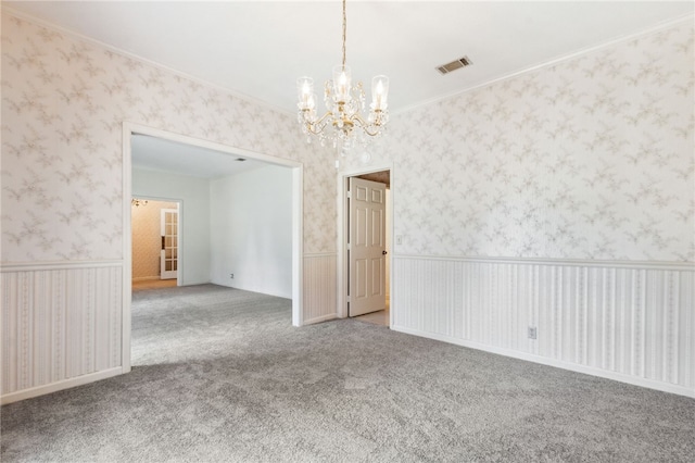 empty room with carpet, crown molding, visible vents, wainscoting, and wallpapered walls