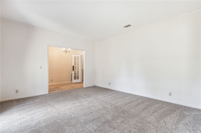 carpeted empty room with visible vents and a notable chandelier