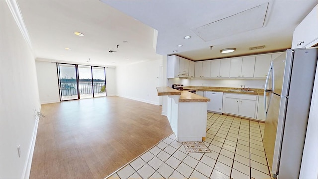 kitchen with a sink, stainless steel electric stove, open floor plan, freestanding refrigerator, and white cabinets