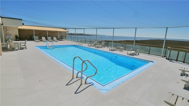 community pool with a water view, fence, and a patio area