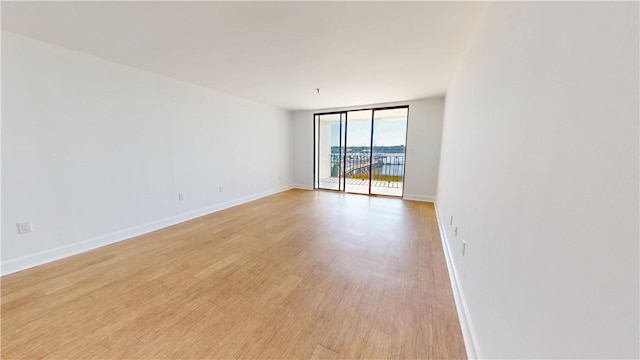 unfurnished room with floor to ceiling windows, light wood-style flooring, and baseboards