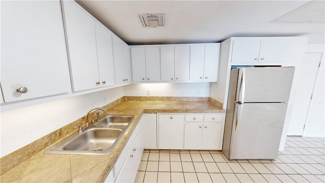 kitchen with visible vents, a sink, freestanding refrigerator, white cabinets, and tile counters