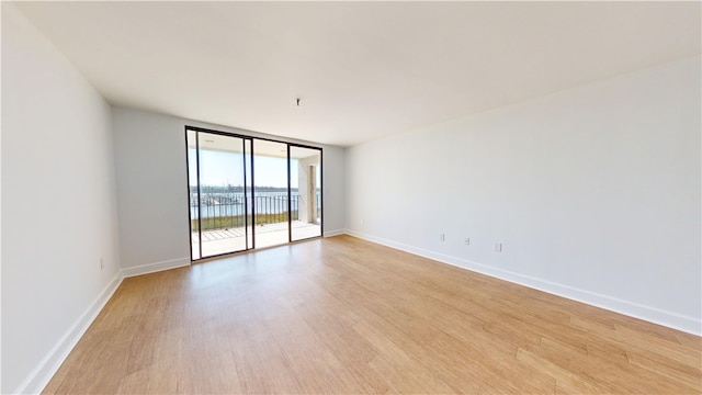 empty room with floor to ceiling windows, light wood-style floors, and baseboards