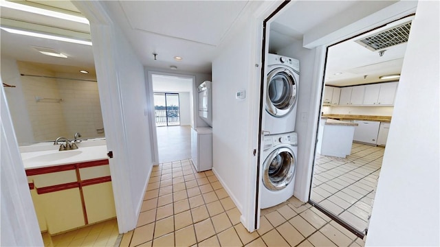 laundry area featuring visible vents, light tile patterned floors, laundry area, stacked washing maching and dryer, and a sink