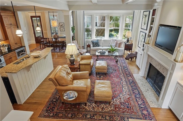 living area with decorative columns, light wood-type flooring, and a fireplace