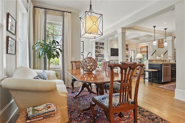 dining room featuring light wood-type flooring, ornate columns, ornamental molding, and a healthy amount of sunlight