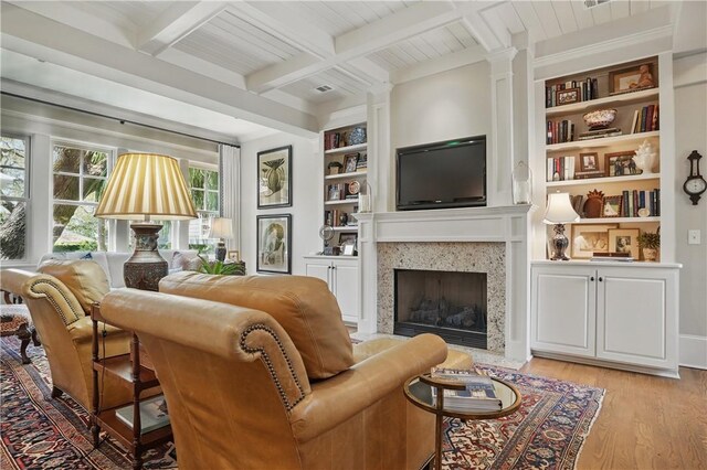 living area with a premium fireplace, beamed ceiling, light wood finished floors, decorative columns, and built in features