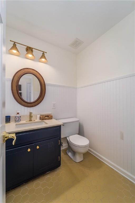 half bathroom with tile patterned floors, visible vents, toilet, vanity, and wainscoting