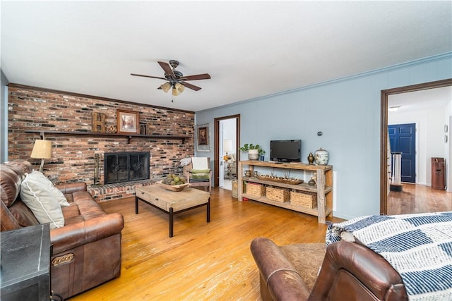 living room with crown molding, a ceiling fan, a brick fireplace, and light wood-style flooring