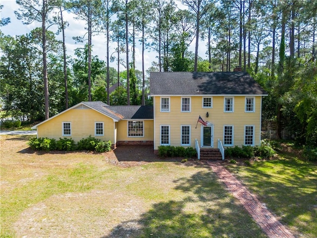 colonial house with a chimney, a front lawn, and roof with shingles