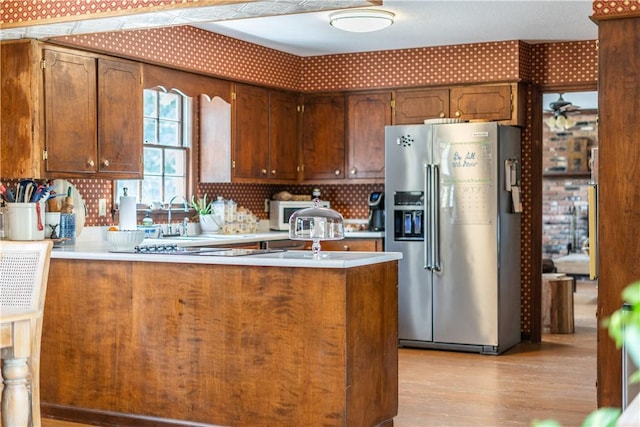 kitchen with a peninsula, a sink, wallpapered walls, stainless steel refrigerator with ice dispenser, and light countertops