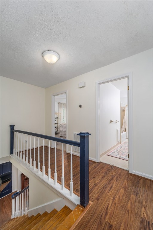 corridor featuring baseboards, wood finished floors, and a textured ceiling
