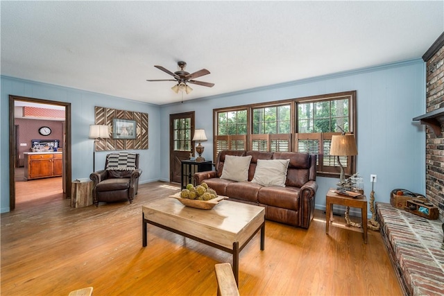 living area featuring light wood finished floors, a ceiling fan, a fireplace, and a healthy amount of sunlight