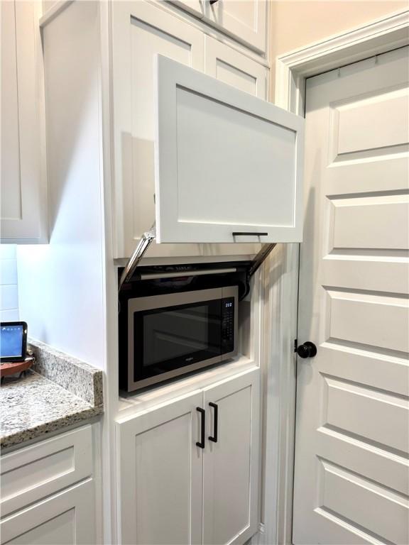 details with stainless steel microwave, white cabinets, light stone countertops, and tasteful backsplash