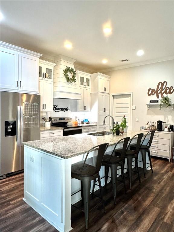 kitchen with a kitchen island with sink, a sink, stainless steel appliances, a breakfast bar area, and light stone countertops