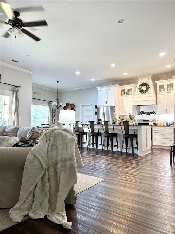 living area featuring dark wood-type flooring, recessed lighting, visible vents, and ornamental molding